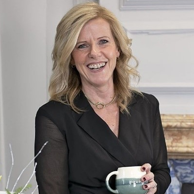 Head and shoulders portrait of Alice Duffy holding a mug and smiling