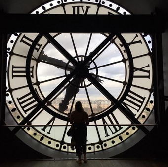 A woman stands in front of the massive clock face at the Musee de Orsay in Paris