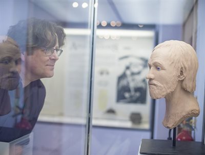 Side shot of a man&amp;#39;s face and a sculpted bust inside a glass case facing each other