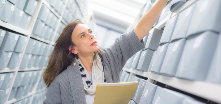 Woman in archive room reaching for documents on shelves