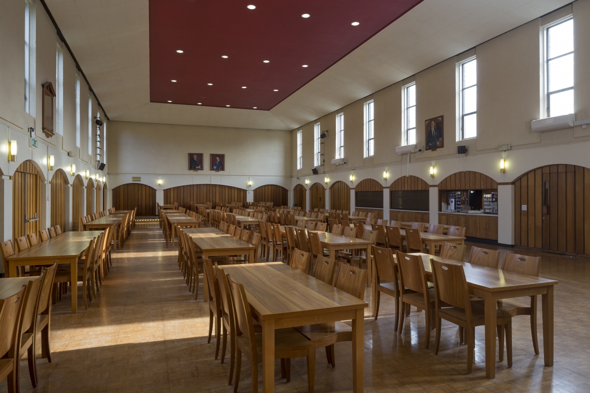 A long open dining hall with tables and chairs through the center.