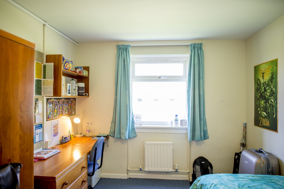 A student bedroom with a desk and wardrobe on one side and single bed on the other.