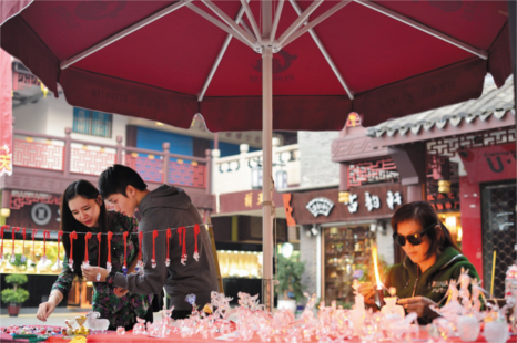An asian couple and an older asian lady browse a stall's offerings in a traditional chinese market