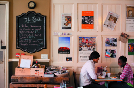 A couple sit in a european style cafe drinking coffee with posters of continental destinations adorning the walls