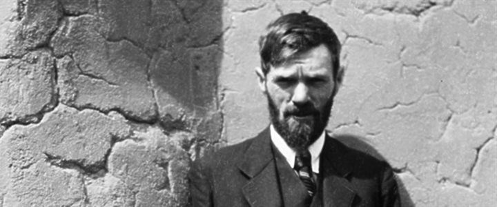Black and white photograph of a white man in a suit with a full beard in front of a textures concrete wall (DH Lawrence)