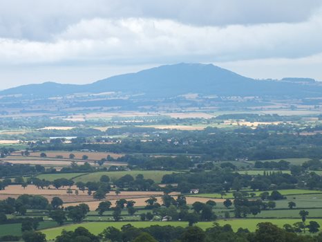 Landscape photo of a large hill beyond trees and farmland