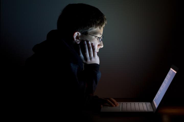 Young person looking into a laptop screen in a dark room