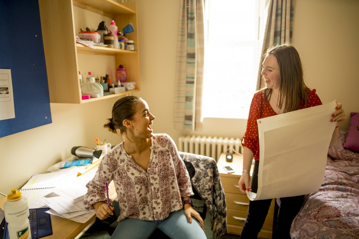 Two students laughing together while decorating a bedroom with posters and personal items