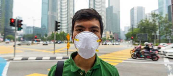 Man wearing a face mask standing in front of a busy road