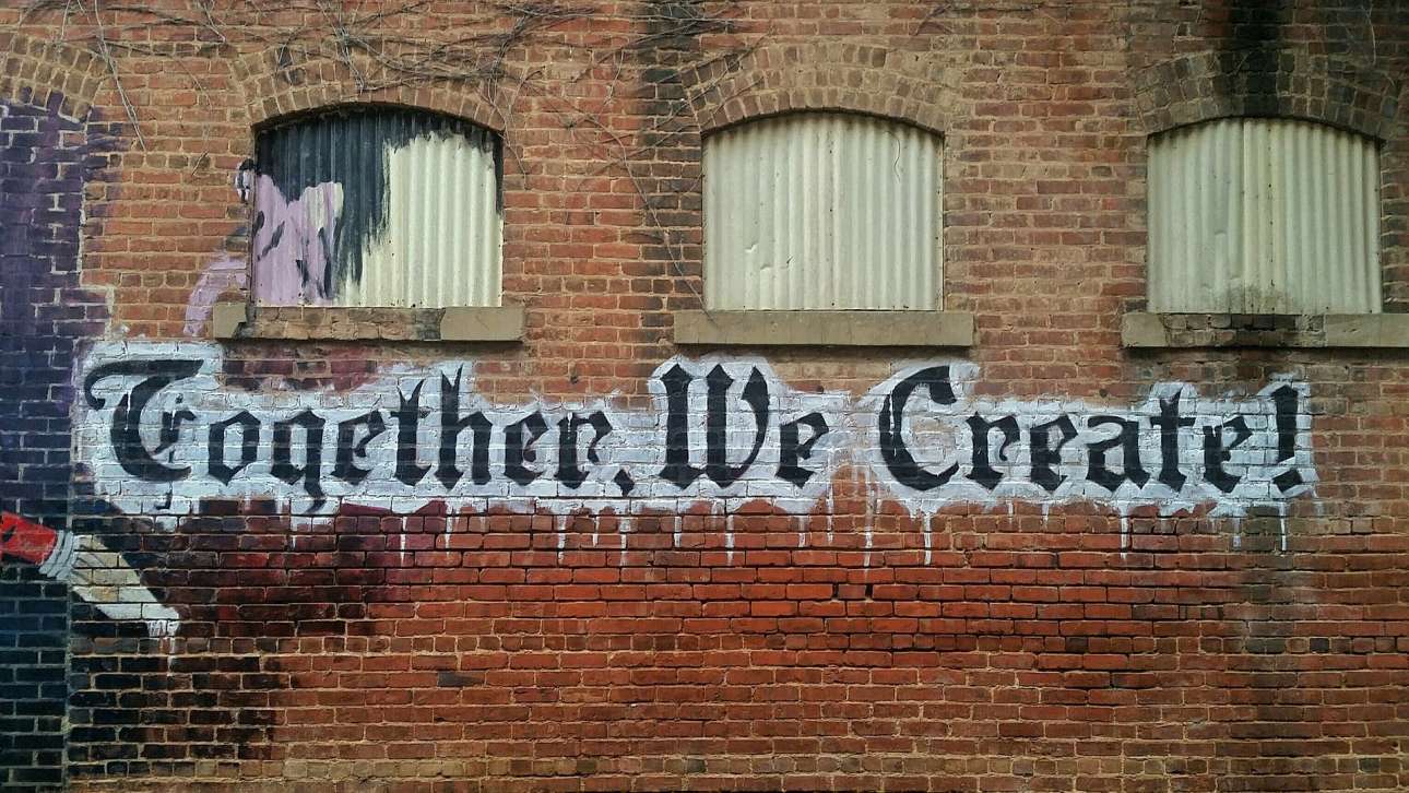 A brick wall with the words 'Together, we create' spray painted onto it