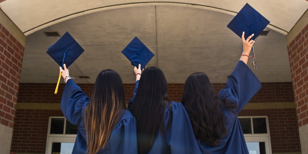 Rear view of graduates dressed in gowns holding caps in air
