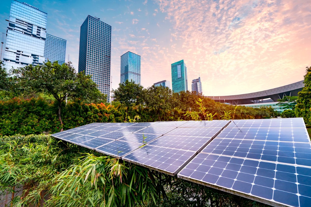 Solar panels in an urban areas surrounded with trees in the foreground and skyscraper buildings in the background.