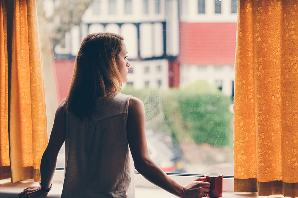 Woman drinking tea and looking out of her window