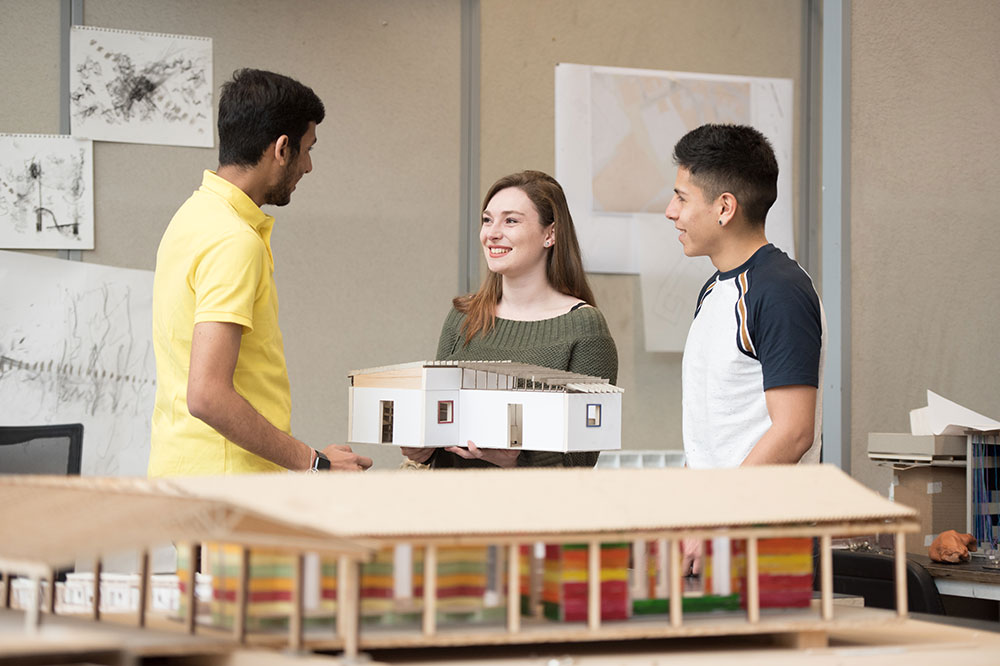 Three students working in a design studio with a house model.