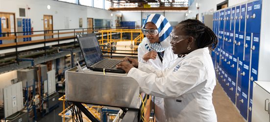 Two female technicians working on a laptop in a workshop