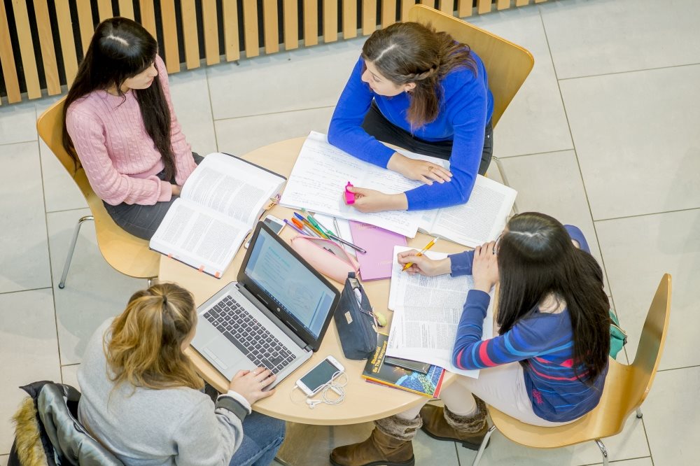 Overhead shot of a group of female students sat round a table in the Humanities atrium