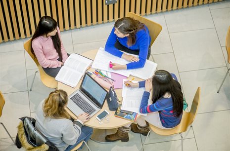 Bird's eye view of students sat round a table talking to an advisor.
