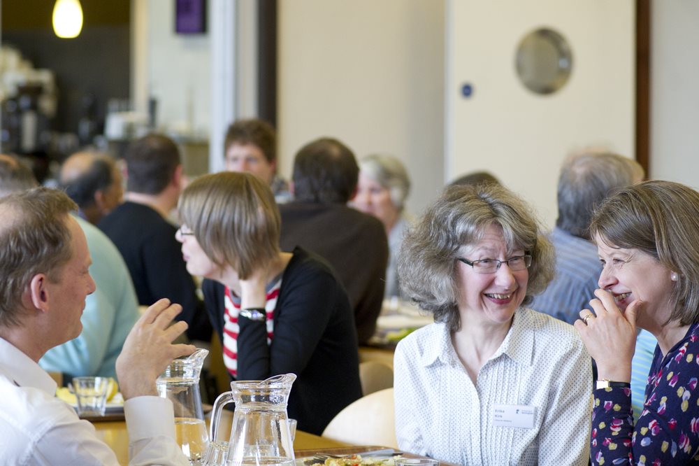 Group of older people with grey hair sat in a café smiling and engaged in lively conversation.