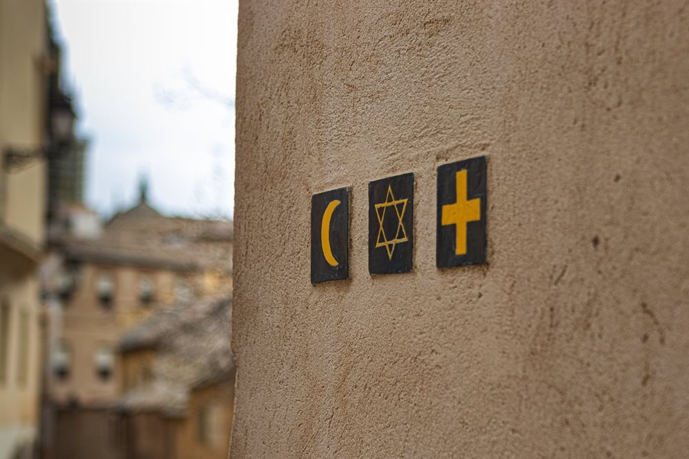 Three square boxes, containing religious symbols on an old rendered cream wall with old buildings in the background.