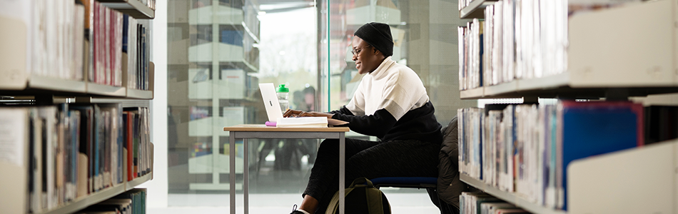 Student working at a desk in the Business Library. Bookshelves are located to either side of the desk.
