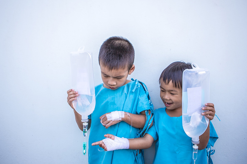 Two children in hospital gowns holding an IV bag