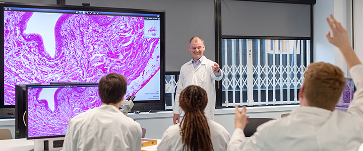 Students in lab coats being taught about cells by a university professor in a specialised lab
