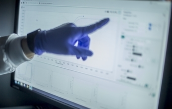 A hand wearing a blue glove pointing to data on a PC screen