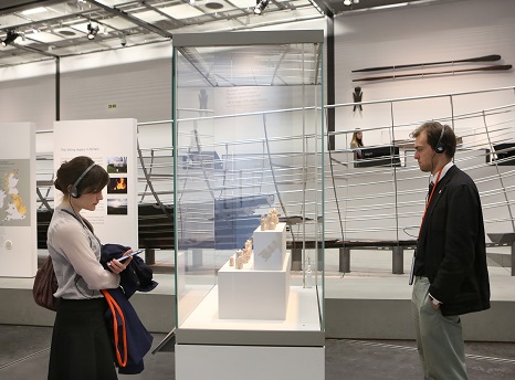 A woman and a man stand either side of a glass case looking at the contents within. Behind them are other museum displays against white walls.