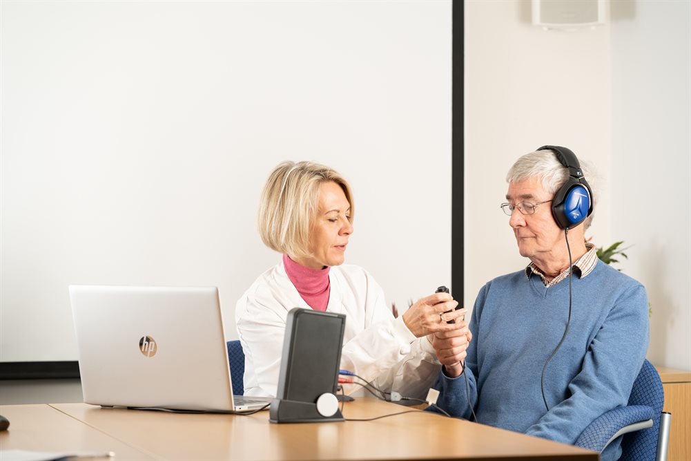 A female researcher guides a male participant wearing headphones through a study