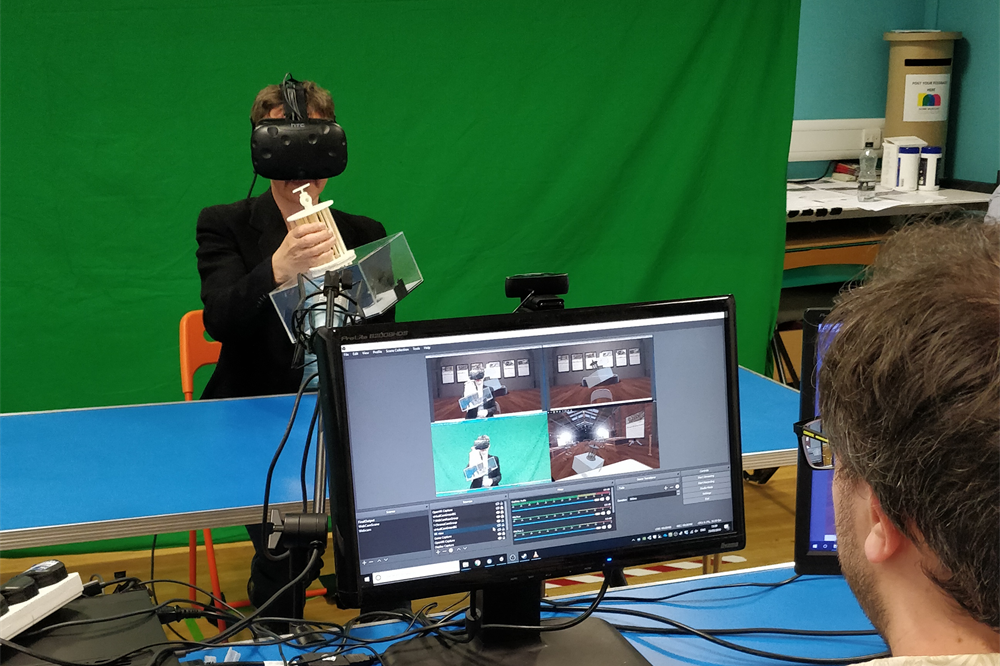A participant uses the VRtefact system—wearing a VR headset—in front of a green screen, while a researcher watches them