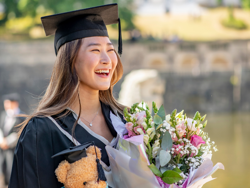 Photograph of a graduate holding a bunch of flowers and smiling at the camera