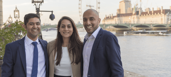 Three people smiling for a photograph in front of the River Thames, London