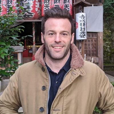 Andrew Schafer standing outside a temple and smiling, wearing a brown coat