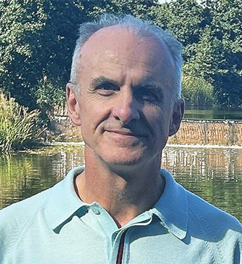 Photo of Professor Marek Korczynksi. Marek is stood outside with trees and a lake visible in the background