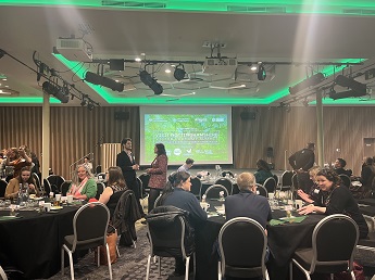 Photo of the conference room for the Visit Nottinghamshire Visitor Economy Summit. People are sat around tables in a conference room with a screen which is displaying the name of the summit.