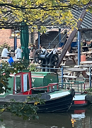 A canal-side cafe with canal boats in the foreground and tables in the background. 