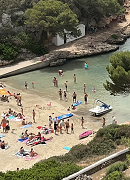 Aerial view of people on a beach cove, which is flanked on both sides by rocks and trees.