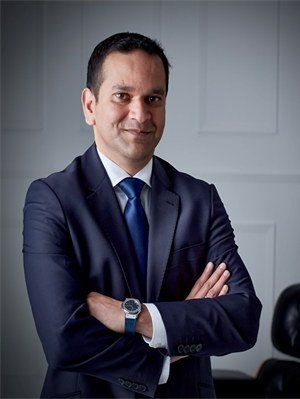 Photo of Arvind Balan, CFO of Rolls Royce Aerospace. Arvind is wearing a dark blue suit with a white shirt and blue tie. He is standing with his arms crossed and smiling.