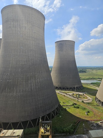 Two concrete cooling towers from Ratcliffe-on-Soar power station. The photo is taken from a height, looking across at the towers which are wider at the bottom and narrower at the top with a curved slope. It's a sunny day with blue skies and minimal cloud.