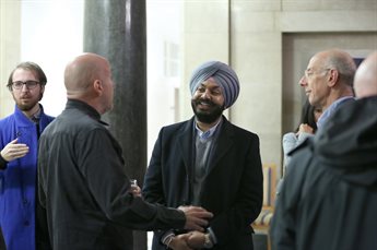 A male delegate wearing a turban stands in the middle of a networking event talking to a mentor. He smiles and appears comfortable and relaxed. Other delegates stand around them, listening to the conversation or talking to each other.