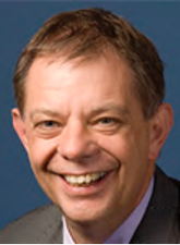 Head and shoulders photo of Andrew Jennings. Andrew is smiling and wearing a white shirt and a grey jacket. The background colour is blue.