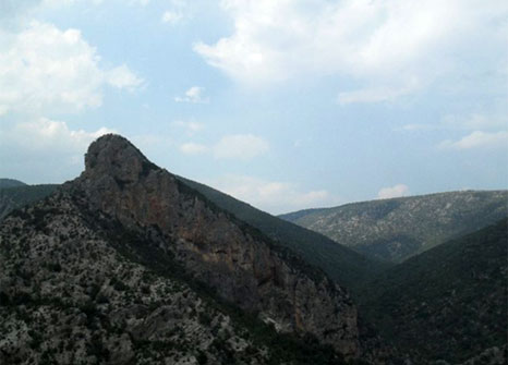 Dark craggy hill silhouetted against blue sky with clouds