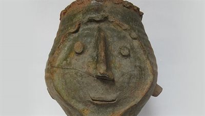 A smiling face carved into a dark grey pot on a grey background