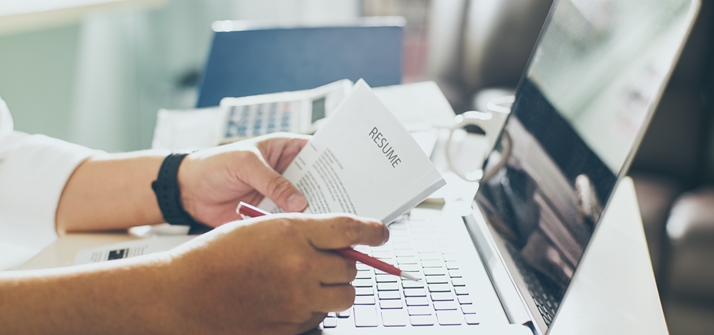 Image of man holding application paperwork in front of laptop