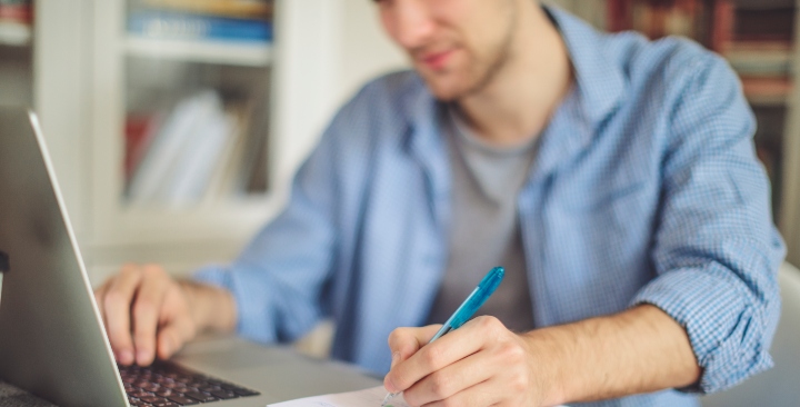 Man making notes while looking at a laptop