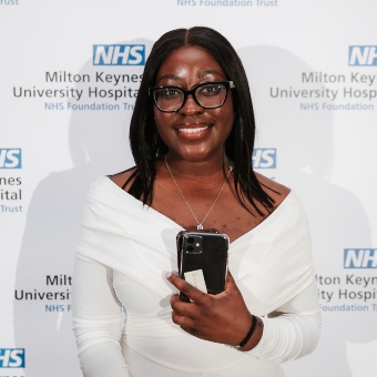 Lilly Koranteng standing in front of a board with the logo on NHS Milton Keynes University Hospital