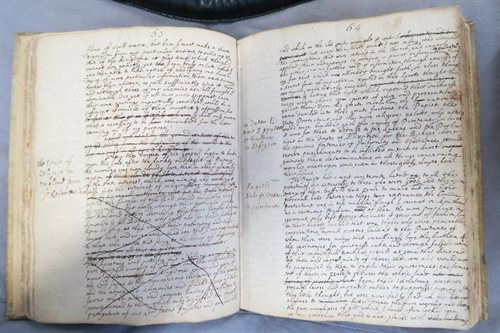 A photograph of an open book. The pages are handwriting with crossings out and annotations.