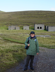 Judith Jesch standing in a field and smiling in front of some brick ruins