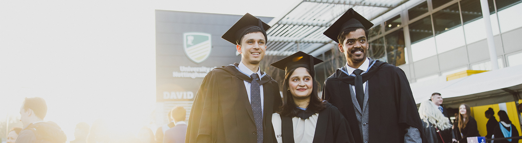 Three students in gowns at graduation, smiling and happy