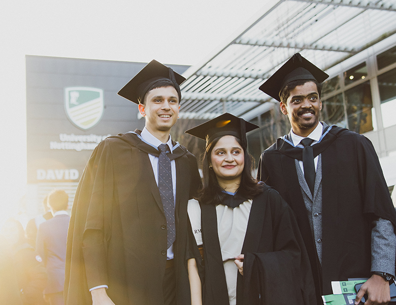 Three students in gowns at graduation, smiling and happy